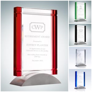 May include: A clear glass retirement award with red accents and a gray base. The award is rectangular and features the text "RETIREMENT AWARD" and "JEFFREY PLANTER". Additional awards with green, black, clear, and blue accents are also shown.