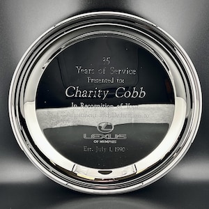 Może przedstawiać: Okrągła, srebrna nagroda z odblaskową powierzchnią. Na szkle wygrawerowano tekst "35 Years of Service" i "Charity Cobb". Widoczne jest również logo Lexusa i data "Est. July 1, 1990".