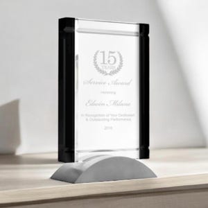 May include: A clear glass service award with black side accents and a gray base. The award reads "15 YEARS Service Award" and honors Edwin Milane for dedicated performance in 2016.