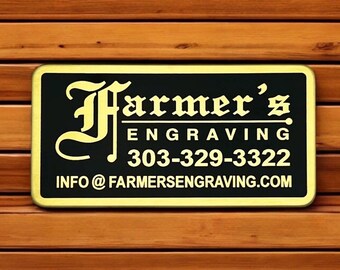 Puede incluir: Un letrero rectangular negro con borde dorado que presenta el texto dorado Farmer's ENGRAVING, el número de teléfono 303-329-3322 y la dirección de correo electrónico INFO@FARMERSENGRAVING.COM en una fuente clara y negrita con una F decorativa.