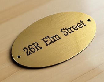 Puede incluir: Una placa de casa ovalada de latón cepillado con el texto negro grabado 26R Elm Street. La placa de metal tiene dos pequeños orificios de montaje circulares, uno en el extremo izquierdo y otro en el derecho, diseñados para una fijación segura.