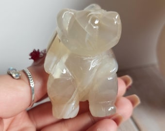 Könnte beinhalten: Eine weiße Achat-Bärenfigur. Der Bär steht auf allen Vieren und hat ein detailliertes Gesicht. Die Figur ist glatt und poliert.