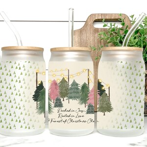 May include: Frosted glass can-shaped tumbler with a bamboo lid and a clear straw. The tumbler features a Christmas tree design with a forest scene and the text "Decked in Joy, Rooted in Love, A Forest of Christmas Cheer."