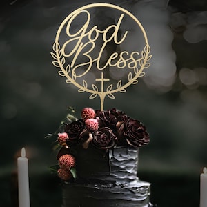 K&ouml;nnte beinhalten: Eine schwarze Hochzeitstorte mit roten und burgunderfarbenen Blumen, die mit einem goldenen Holz-Tortenaufsatz verziert ist, auf dem "God Bless" mit einem Kreuz und Bl&auml;ttern steht.
