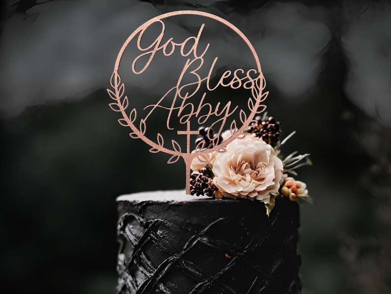 K&ouml;nnte beinhalten: Ein schwarzer Kuchen mit einer Rose und Beeren darauf. Ein Holzaufsatz mit den Worten "God Bless Abby" und einem Kreuz befindet sich oben auf dem Kuchen.