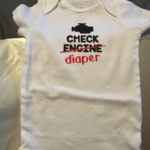May include: White baby onesie with a black check engine light graphic and the text "CHECK ENGINE" crossed out with a red line and the word "diaper" written below.