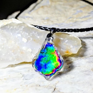 May include: A teardrop-shaped iridescent glass pendant necklace with a black braided cord. The pendant has a rainbow of colors, including blue, green, and yellow.