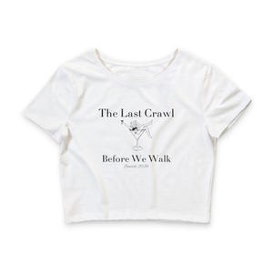 Puede incluir: Top corto blanco con el texto "The Last Crawl Before We Walk Seniors 2026" en negro. También hay un dibujo de una persona en una copa de martini en la camiseta. La camiseta tiene mangas cortas y cuello redondo.