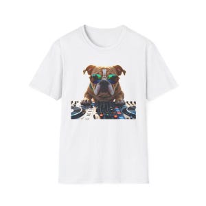 May include: White t-shirt with a digital illustration of a brown bulldog wearing sunglasses, positioned behind a DJ mixing console. The design is a fun, eye-catching graphic, ideal for music fans and dog lovers.
