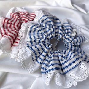 May include: Two fabric hair scrunchies with white lace trim. One scrunchie is red and white striped, the other is blue and white striped.