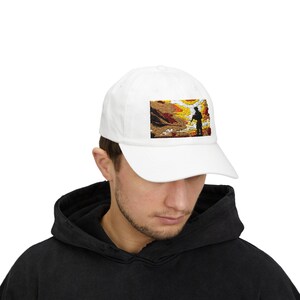 May include: White baseball cap with an embroidered image of a person standing in a landscape with a sunset. The landscape is a mix of yellow, orange, and red.