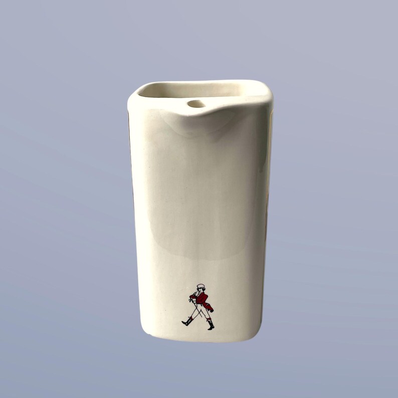 Peut inclure: Pichet en c&eacute;ramique blanche de forme carr&eacute;e avec un bec verseur. Le pichet a un logo d'un homme marchant imprim&eacute; sur le devant.