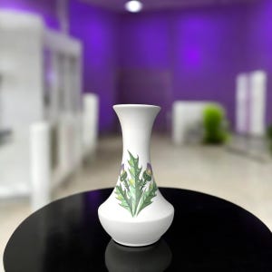 May include: A white ceramic vase with a flared neck and a rounded base, featuring a decorative illustration of green thistle leaves and purple thistle flowers centered on the front surface of the vessel.