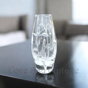 May include: A clear glass vase with an etched design of white flowers. The vase has a rounded bottom and a narrow neck.