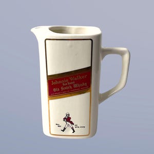 Peut inclure: Pichet en c&eacute;ramique blanche avec une bordure dor&eacute;e et une &eacute;tiquette Johnnie Walker Red Label Old Scotch Whisky rouge et dor&eacute;e. L'&eacute;tiquette repr&eacute;sente un homme en manteau rouge marchant avec une canne. Le texte sur l'&eacute;tiquette indique "N&eacute; en 1820, toujours en pleine forme."