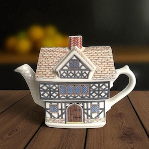 Peut inclure: Théière décorative en céramique blanche en forme de maison de style Tudor. Le toit est brun, avec des colombages noirs et blancs et des fenêtres bleues. La poignée et le bec sont blancs.