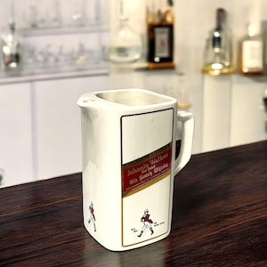 May include: White ceramic jug with a Johnnie Walker Red Label Old Scotch Whisky logo. The jug has a gold trim and a handle.