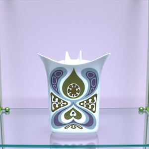 May include: A white ceramic vase with a flared top and two small vertical protrusions. The body features a symmetrical graphic pattern in shades of olive green, light blue, and muted purple, creating a repeating organic design on the front.