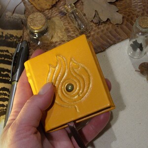 May include: A small, yellow leather-bound journal with a decorative embossed design of a flame. The journal has a brown ribbon bookmark.