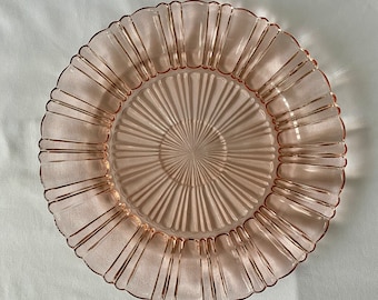 Puede incluir: Un plato de vidrio rosa con un borde acanalado y un patrón de sol en el centro.