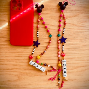 May include: Two phone straps with Mickey Mouse charms. Each strap features a variety of colorful beads, including pink, yellow, blue, and green. The straps also include white letter beads that spell out "ENJOY".