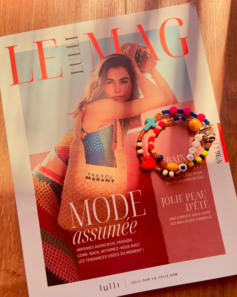 Puede incluir: Una portada de revista con el t&iacute;tulo "LE MAG" y el texto "MODE assum&eacute;e" en letras grandes y en negrita. La portada presenta a una mujer con un top de crochet de colores y un bolso de paja con el texto "ISABEL MARANT". La revista est&aacute; sobre una superficie de madera con una pulsera de cuentas de colores con abalorios.