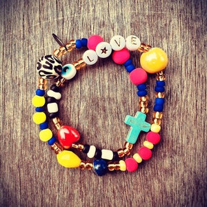 Puede incluir: Pulsera de cuentas multicolores con un dije de cruz, un dije de coraz&oacute;n, un dije de ojo turco y un dije que dice "LOVE" con una estrella.