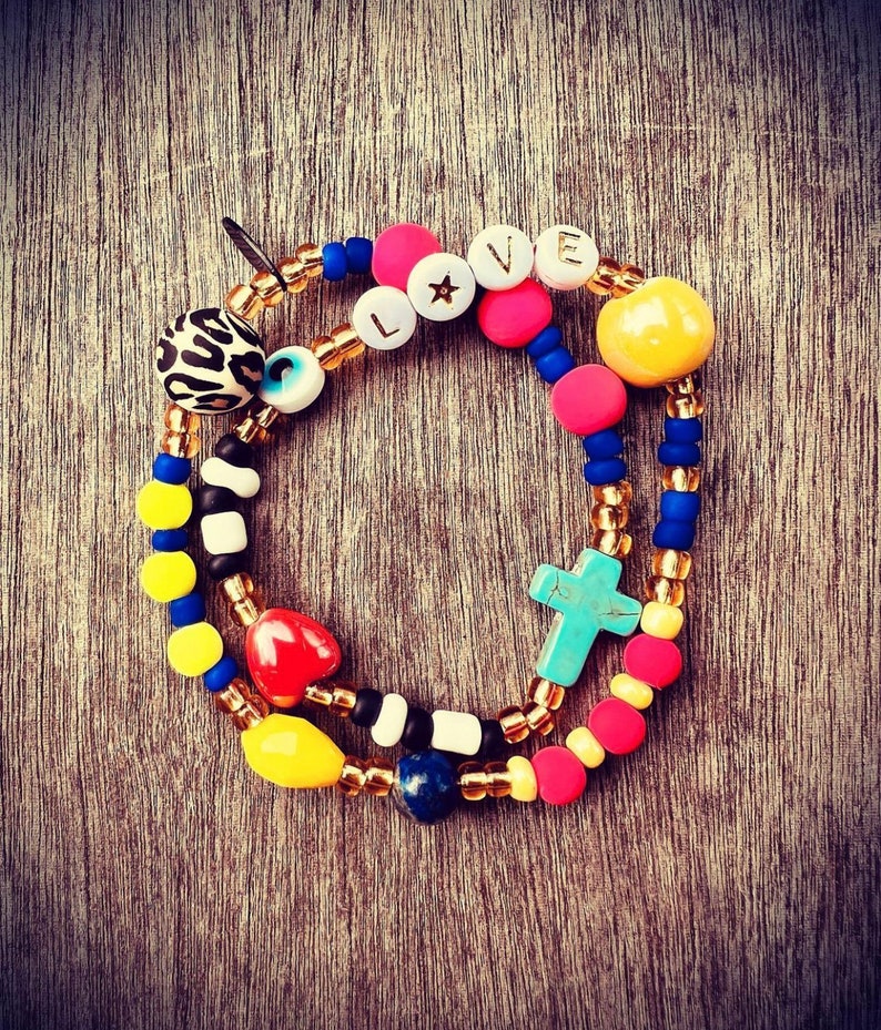 Puede incluir: Pulsera de cuentas multicolores con un dije de cruz, un dije de coraz&oacute;n, un dije de ojo turco y un dije que dice "LOVE" con una estrella.