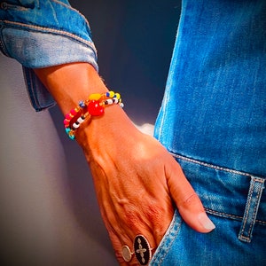 Puede incluir: Una persona lleva un vestido de mezclilla con un brazalete de cuentas de colores en la mu&ntilde;eca y un anillo con una cruz negra en el dedo.