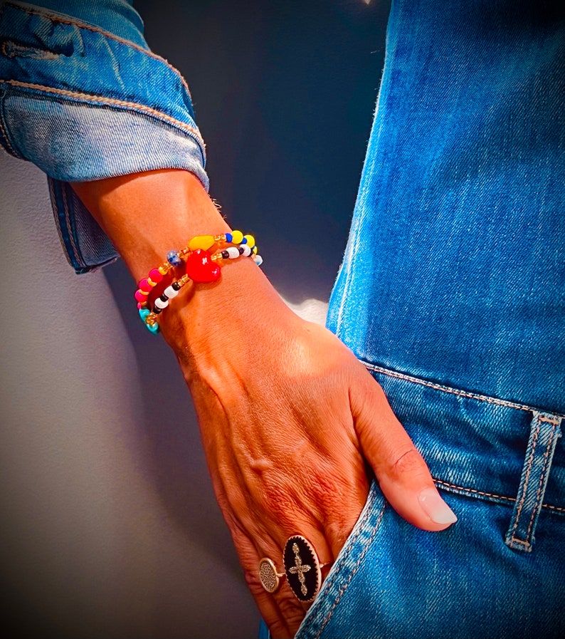 Puede incluir: Una persona lleva un vestido de mezclilla con un brazalete de cuentas de colores en la mu&ntilde;eca y un anillo con una cruz negra en el dedo.