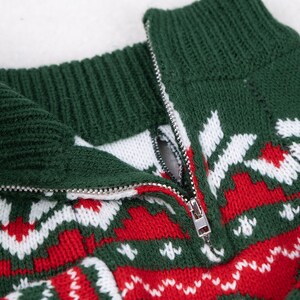 May include: Close-up of a green, red, and white knitted sweater with a half-zip closure. The sweater features a festive pattern with snowflakes and geometric shapes. The zipper is silver.