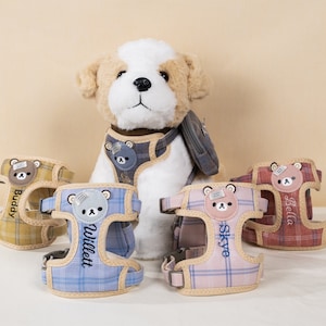 May include: Four personalized dog harnesses with different plaid patterns and embroidered names: Buddy, Willett, Skye, and Bella. Each harness features a small bear applique.