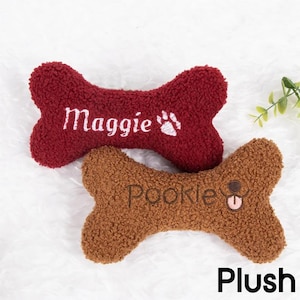 Op de afbeelding: Twee pluche hondenbot speelgoed. E&eacute;n is bordeauxrood met wit geborduurd "Maggie", samen met een pootafdruk. De andere is bruin met bruin geborduurd "Pookie", met een honden gezicht. Het woord "Plush" staat onderaan.
