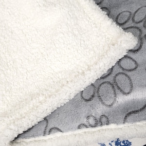 May include: A soft, white sherpa blanket with a gray fleece side featuring a pattern of circles. The blanket is folded in half, showing both sides.