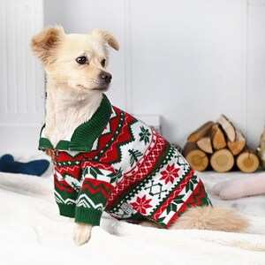 May include: A small dog wearing a festive Christmas sweater. The sweater features a red, white, and green pattern with snowflakes, trees, and geometric designs. The sweater has a green collar and a zipper closure.
