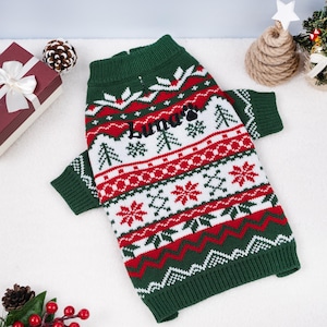 May include: A green, red, and white Christmas-themed dog sweater. The sweater features a pattern of snowflakes, trees, and zigzags. The name "Luna" is embroidered on the front. The sweater has a high collar and sleeves.