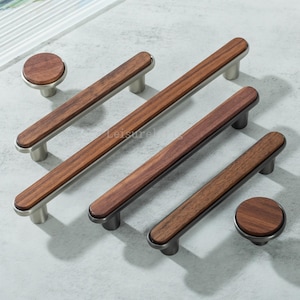 May include: A selection of wooden cabinet handles and knobs. The handles feature a dark wood centre and brushed metal ends. The knobs are circular with matching wood grain. The hardware is designed for furniture, with measurements in centimetres.