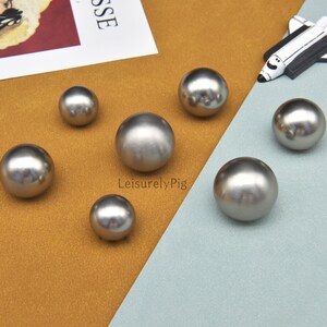May include: A collection of seven shiny, silver-colored metal spheres of varying sizes. The spheres are arranged on a surface with a brown and blue color scheme. The image also includes a small decorative airplane.