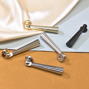 Puede incluir: Un conjunto de tiradores de armario en dorado, plateado y negro. Cada tirador presenta un mango acanalado y una base redonda. Los tiradores están dispuestos sobre un fondo neutro con una tela satinada.