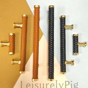 Puede incluir: Una selección de tiradores de armario con un diseño de cuero trenzado en marrón y negro. Los tiradores tienen detalles dorados y están dispuestos en un patrón. El texto "LeisurelyPig" es visible en la parte inferior.
