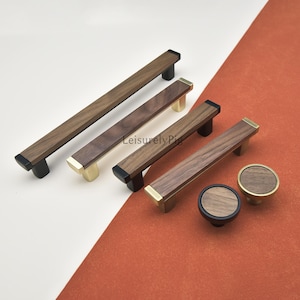 Puede incluir: Una colección de herrajes de madera para gabinetes, que incluye tiradores y pomos. Los tiradores tienen un cuerpo rectangular de madera con detalles en negro o dorado. Los pomos son redondos con una cara de madera y bases negras o doradas. El texto "LeisurelyPig" es visible.