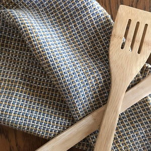 May include: Two wooden kitchen spatulas crossed over a blue and yellow patterned kitchen towel.