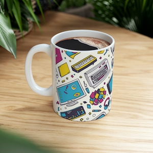 May include: White ceramic mug with a colorful retro computer and technology themed design. The mug is filled with coffee.