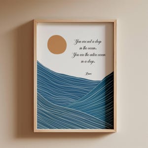 Op de afbeelding: Een ingelijste kunstdruk met een minimalistisch ontwerp. Het kunstwerk bevat een gouden zon, blauwe oceaangolven en de quote "You are not a drop in the ocean. You are the entire ocean in a drop." van Rumi, in elegant schrift.