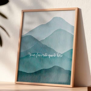 以下が含まれることがあります： 水色と青色のグラデーションで描かれた、山々の風景が特徴の額入り水彩画。作品には筆記体で「Your favorite quote here」というテキストが含まれています。フレームは明るい色の木材で作られています。