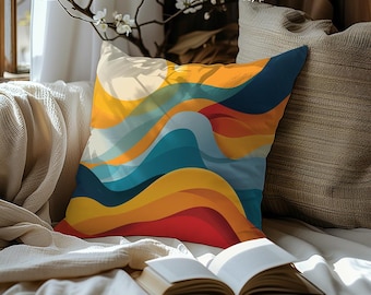 May include: A throw pillow with a colorful abstract design featuring wavy lines in shades of yellow, orange, red, blue, and white. The pillow is on a couch with a book and a plant.