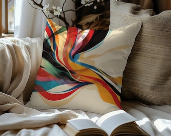 May include: A square decorative pillow with an abstract design featuring flowing lines of red, yellow, blue, and black on a cream background. The pillow is placed on a bed with an open book.