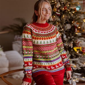 May include: A red, green, white and yellow Christmas jumper with a fair isle pattern. The jumper features a crew neck and long sleeves.