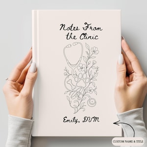 May include: A light-colored notebook featuring the black text Notes From the Clinic and Emily, DVM. The cover displays a black line art illustration of a stethoscope, a paw print, a bone, a pet collar, and floral elements arranged vertically.