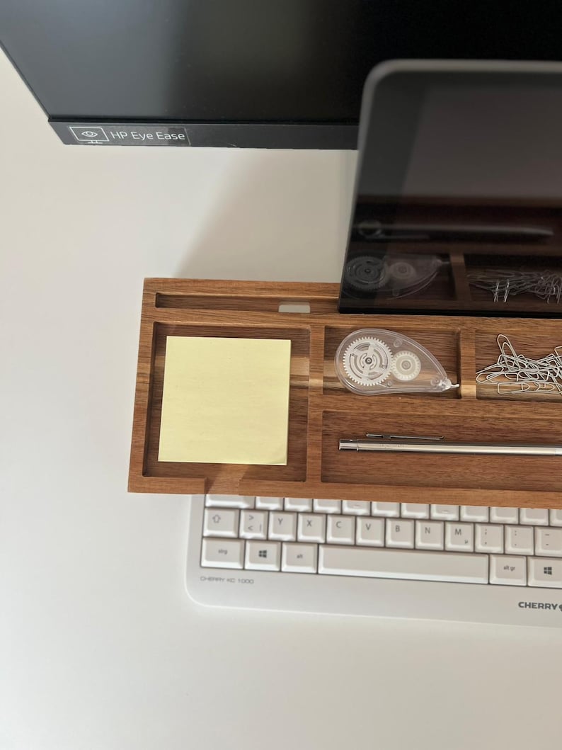 May include: A wooden desk organizer with compartments for office supplies. It holds a yellow sticky note, a white correction tape dispenser, paper clips, and a pen. A white keyboard is below the organizer. The monitor above has "HP Eye Ease" printed on it.